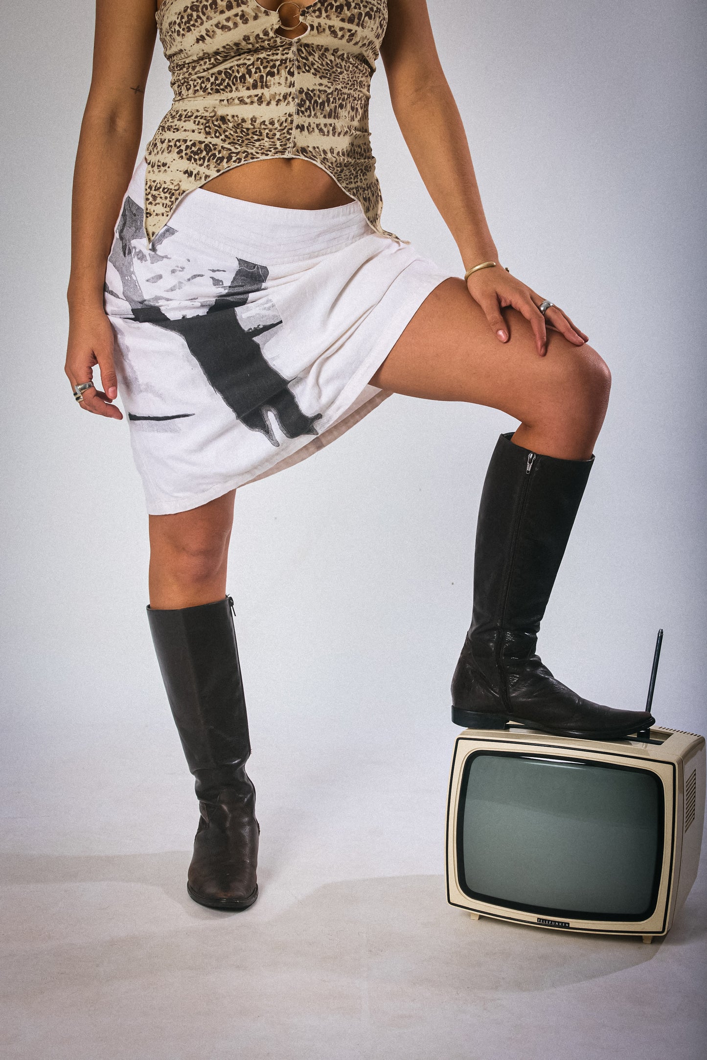 Person wearing a patterned top and white skirt with black graphics, standing on an old television set.