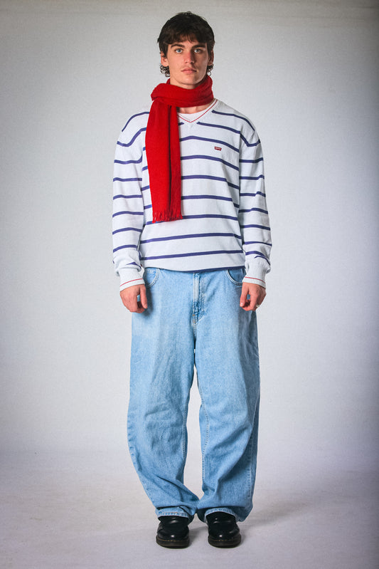 Person wearing a striped sweater, red scarf, and blue jeans on a plain background