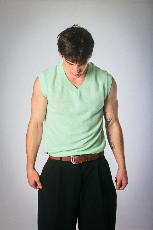 Man wearing a light green sleeveless Asos vest shirt and black pants against a plain background