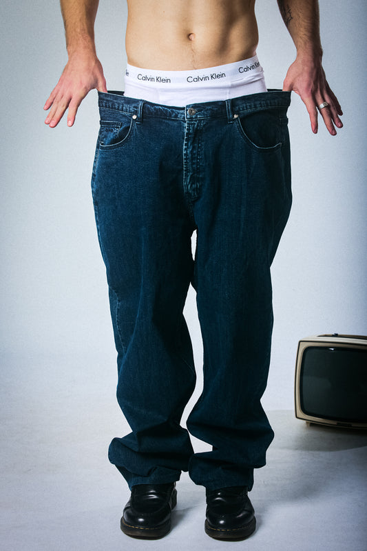 Person wearing dark blue jeans and Calvin Klein underwear on a plain background